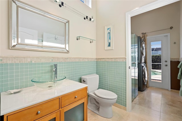 bathroom with stacked washer / drying machine, toilet, tile walls, vanity, and tile patterned flooring