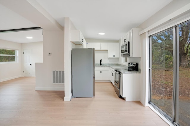 kitchen with white cabinetry, stainless steel appliances, light stone counters, and light wood-type flooring