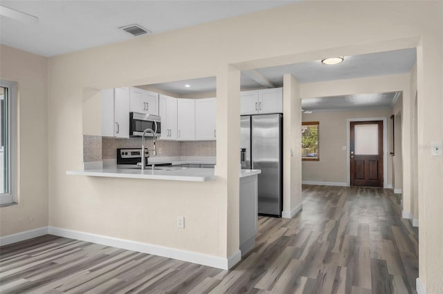 kitchen with appliances with stainless steel finishes, hardwood / wood-style floors, tasteful backsplash, white cabinetry, and kitchen peninsula