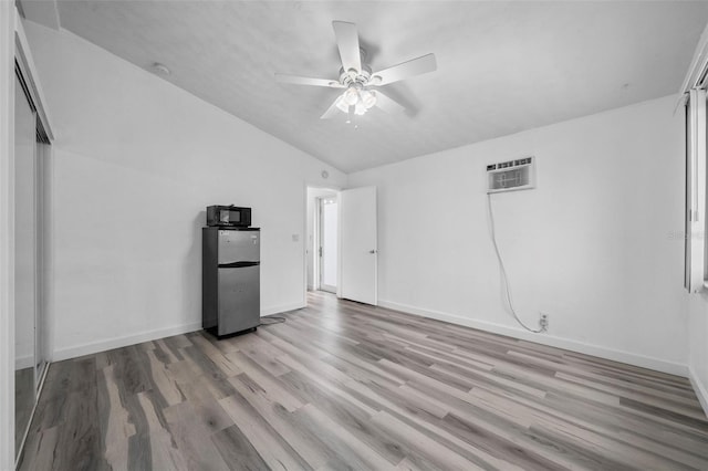 unfurnished room featuring light hardwood / wood-style flooring, an AC wall unit, ceiling fan, and vaulted ceiling