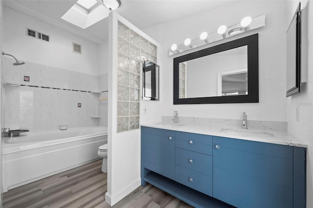 full bathroom with a skylight, wood-type flooring, tiled shower / bath combo, vanity, and toilet