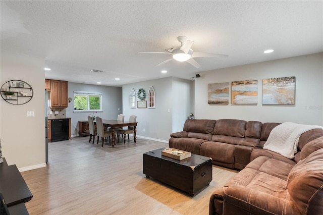 living room with ceiling fan, a textured ceiling, and light wood-type flooring