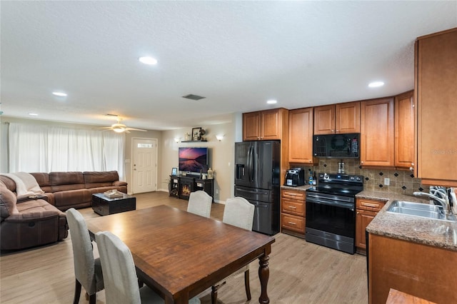 kitchen featuring sink, black appliances, light stone countertops, decorative backsplash, and light wood-type flooring