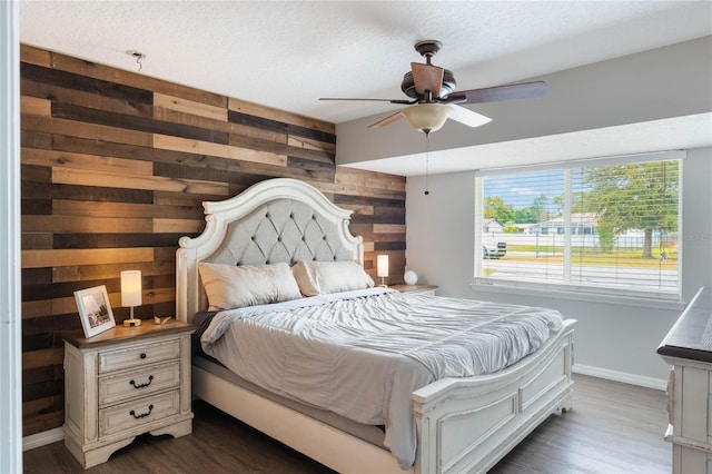 bedroom with dark wood-type flooring, ceiling fan, wooden walls, and a textured ceiling