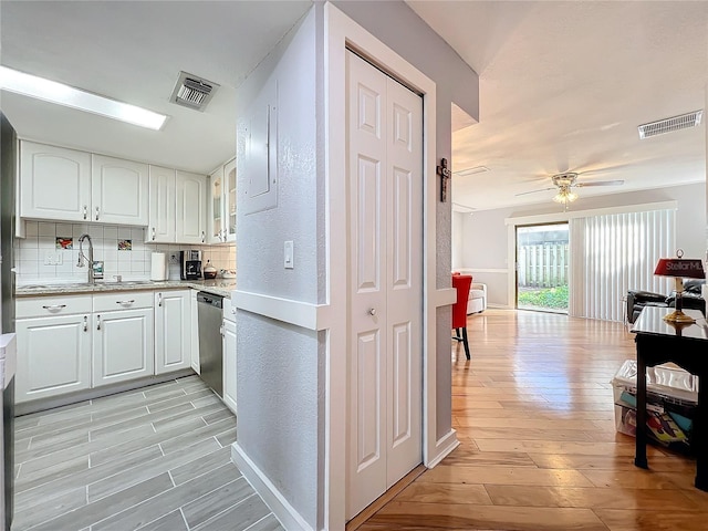 kitchen with tasteful backsplash, dishwasher, sink, white cabinets, and light hardwood / wood-style flooring