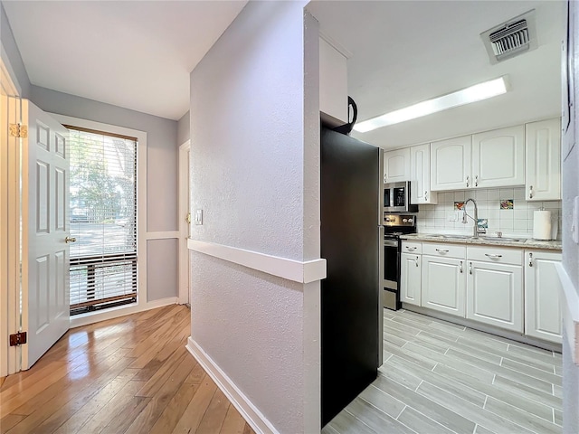 kitchen featuring sink, appliances with stainless steel finishes, white cabinetry, backsplash, and light wood-type flooring