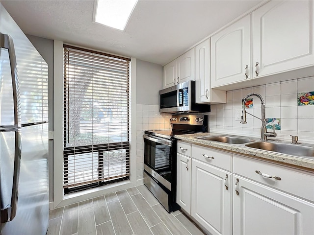 kitchen featuring sink, appliances with stainless steel finishes, tile walls, a textured ceiling, and white cabinets