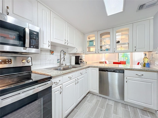 kitchen featuring sink, appliances with stainless steel finishes, backsplash, light stone countertops, and white cabinets