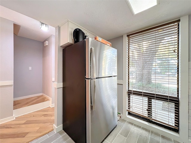 kitchen with stainless steel fridge, a textured ceiling, and light wood-type flooring