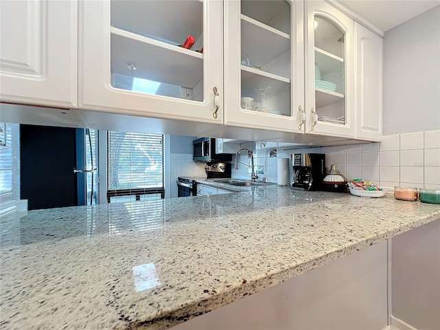 kitchen with tasteful backsplash, light stone countertops, sink, and white cabinets