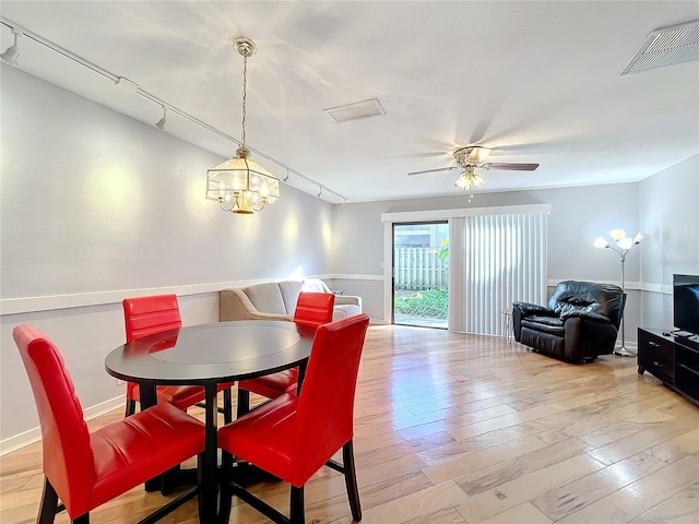 dining area with ceiling fan with notable chandelier, rail lighting, and light wood-type flooring