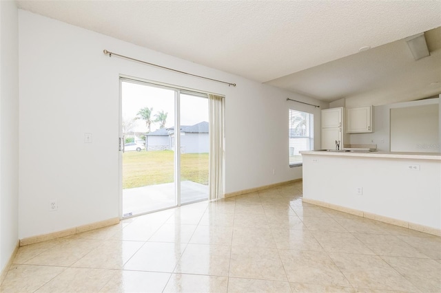 empty room featuring vaulted ceiling, a textured ceiling, and light tile patterned floors