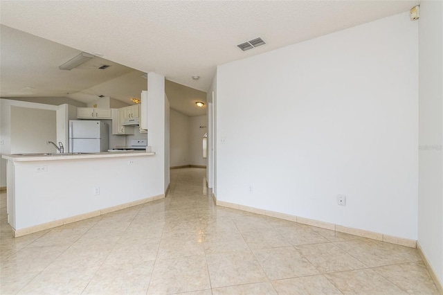 interior space featuring a textured ceiling, kitchen peninsula, white fridge, white cabinets, and stove