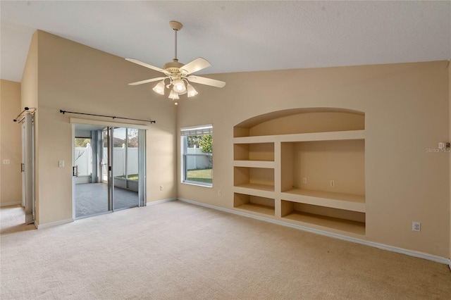 carpeted empty room with lofted ceiling, built in shelves, and ceiling fan