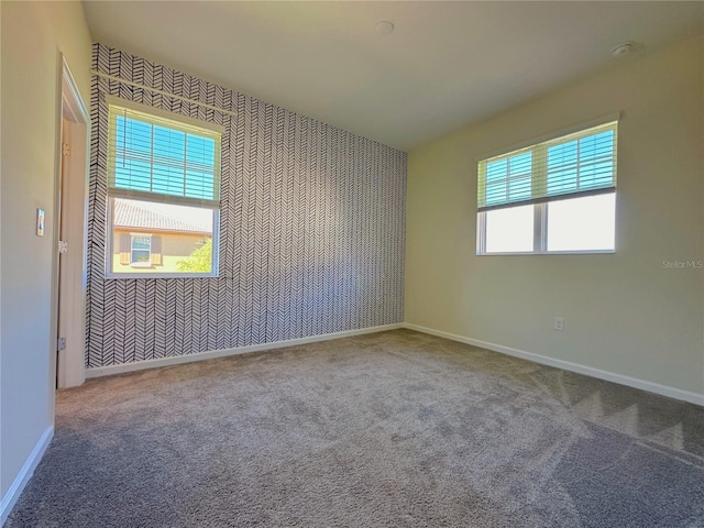 spare room featuring an accent wall, carpet flooring, wallpapered walls, and baseboards