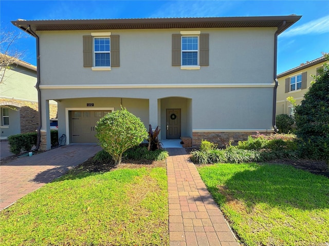 view of front facade featuring stone siding, a front yard, decorative driveway, and stucco siding