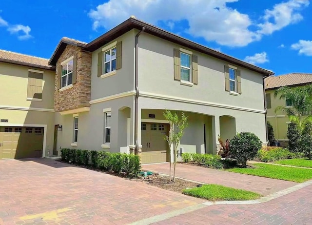 view of front of home with stone siding, decorative driveway, an attached garage, and stucco siding