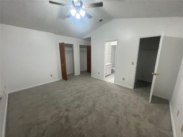 unfurnished bedroom with lofted ceiling, ceiling fan, carpet flooring, ensuite bathroom, and multiple closets