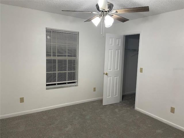 unfurnished bedroom featuring dark colored carpet, a spacious closet, ceiling fan, a textured ceiling, and a closet