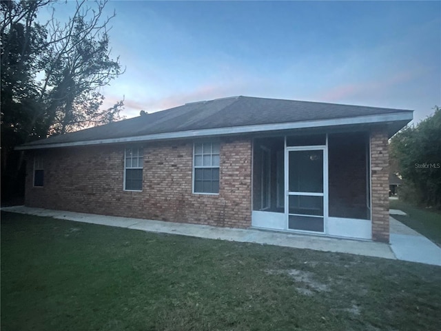 back house at dusk featuring a yard and a sunroom