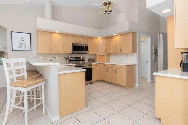 kitchen with appliances with stainless steel finishes, a breakfast bar, high vaulted ceiling, and kitchen peninsula