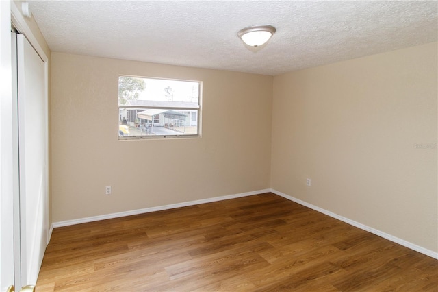 spare room featuring baseboards, a textured ceiling, and light wood finished floors