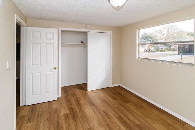 unfurnished bedroom with light wood finished floors, a textured ceiling, baseboards, and a closet