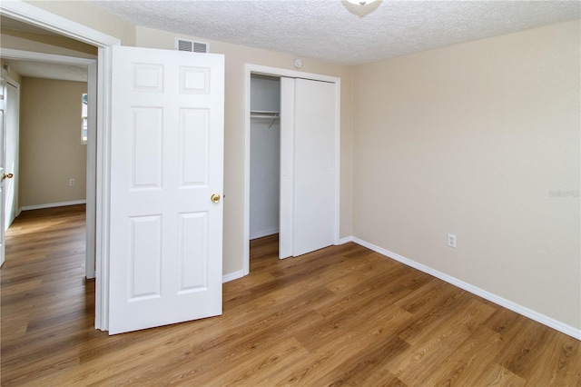 unfurnished bedroom featuring baseboards, visible vents, a textured ceiling, light wood-type flooring, and a closet