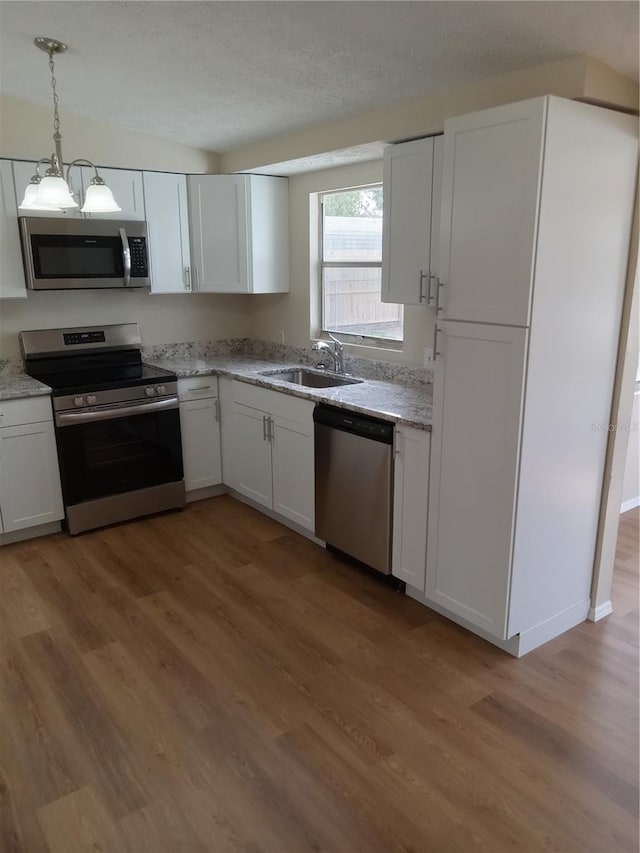 kitchen featuring light wood finished floors, appliances with stainless steel finishes, a sink, and white cabinets