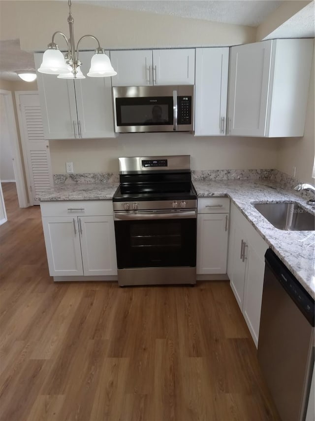 kitchen with light wood finished floors, hanging light fixtures, appliances with stainless steel finishes, white cabinetry, and a sink