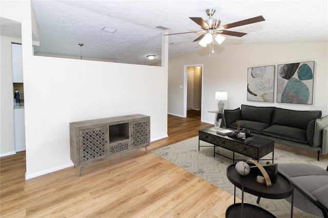 living area with ceiling fan, a textured ceiling, wood finished floors, visible vents, and vaulted ceiling