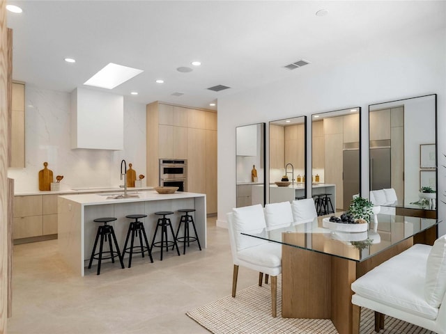 kitchen with sink, a breakfast bar area, double oven, a skylight, and a center island with sink