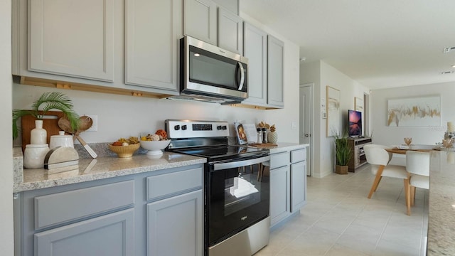 kitchen with gray cabinetry, stainless steel appliances, light stone countertops, and light tile patterned floors