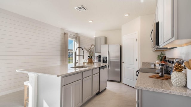 kitchen with sink, appliances with stainless steel finishes, a kitchen island with sink, light stone countertops, and a kitchen bar