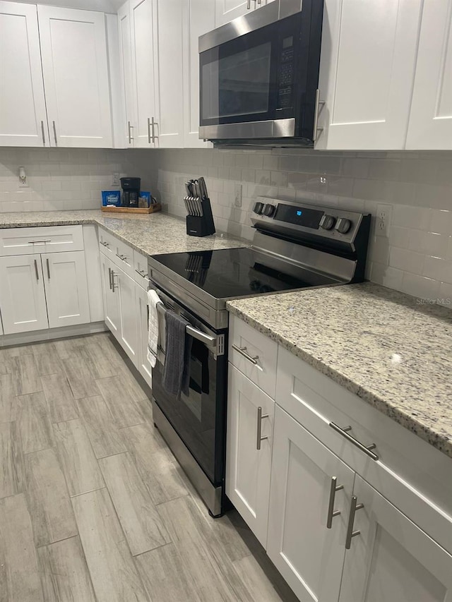 kitchen featuring white cabinetry, light stone countertops, backsplash, and stainless steel appliances