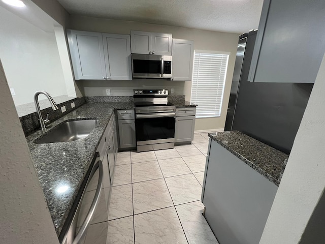 kitchen featuring sink, gray cabinetry, dark stone counters, stainless steel appliances, and a textured ceiling