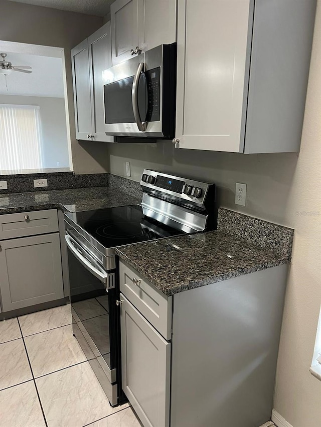 kitchen featuring ceiling fan, appliances with stainless steel finishes, dark stone countertops, gray cabinetry, and light tile patterned flooring