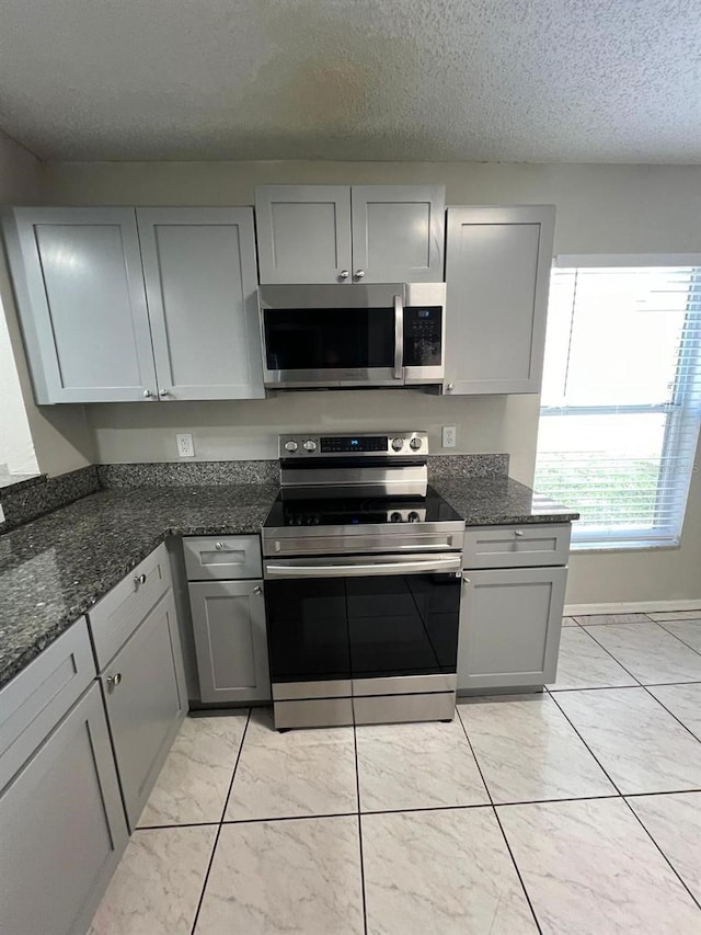 kitchen featuring dark stone countertops, gray cabinets, stainless steel appliances, and a textured ceiling