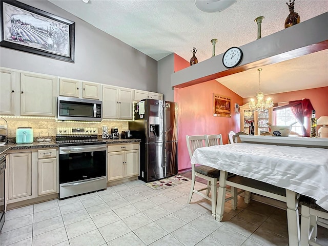 kitchen with lofted ceiling, decorative light fixtures, appliances with stainless steel finishes, decorative backsplash, and cream cabinetry