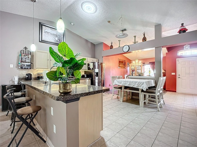 kitchen with stainless steel fridge, hanging light fixtures, a kitchen bar, vaulted ceiling, and kitchen peninsula