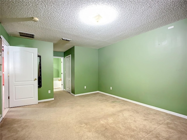 unfurnished bedroom featuring a closet, ensuite bath, light carpet, and a textured ceiling