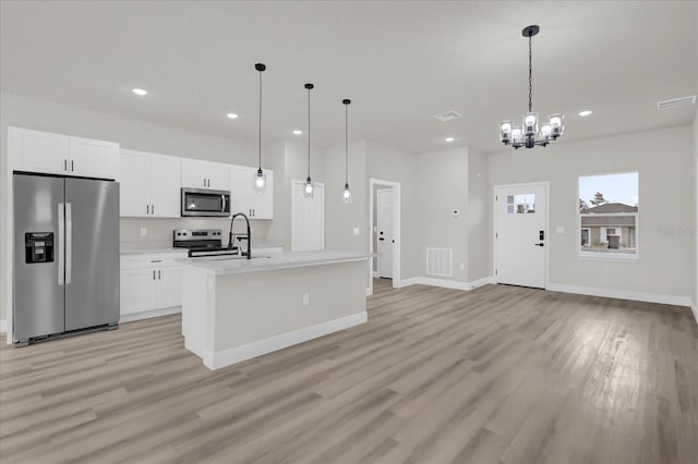 kitchen with white cabinetry, hanging light fixtures, stainless steel appliances, and a center island with sink