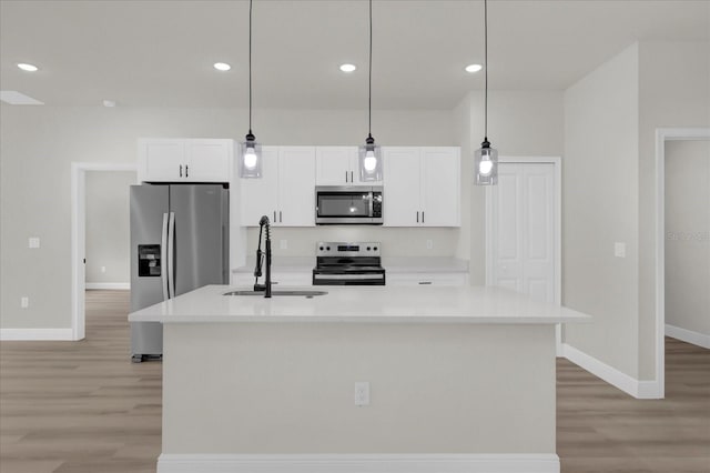 kitchen with sink, appliances with stainless steel finishes, a kitchen island with sink, white cabinetry, and decorative light fixtures