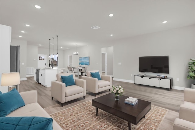 living room with an inviting chandelier, sink, and light hardwood / wood-style flooring