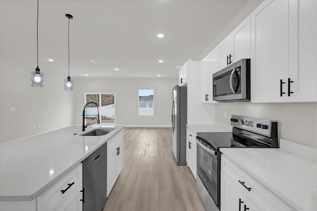 kitchen featuring decorative light fixtures, white cabinetry, sink, stainless steel appliances, and light wood-type flooring