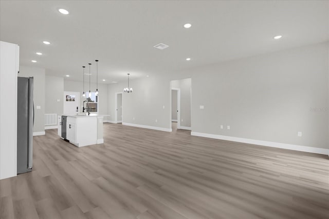 unfurnished living room featuring baseboards, light wood-style flooring, an inviting chandelier, a sink, and recessed lighting