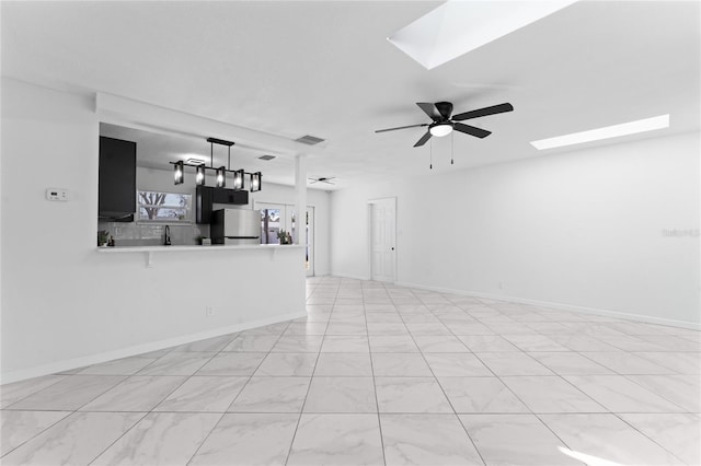 unfurnished living room with ceiling fan and a skylight