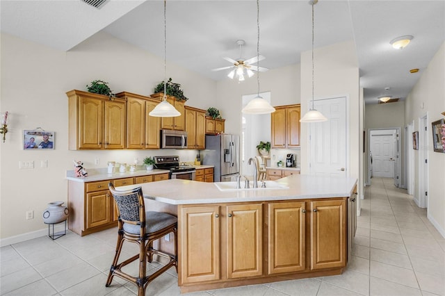 kitchen featuring a breakfast bar, pendant lighting, sink, stainless steel appliances, and a center island with sink