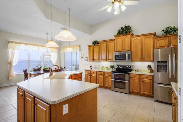 kitchen with sink, hanging light fixtures, stainless steel appliances, a water view, and a center island with sink