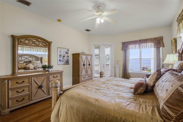 bedroom with dark hardwood / wood-style flooring, access to exterior, ceiling fan, a water view, and french doors